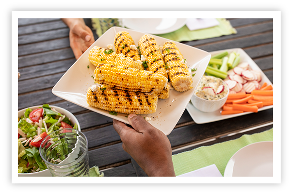 Woman handing man a plate of grilled corn