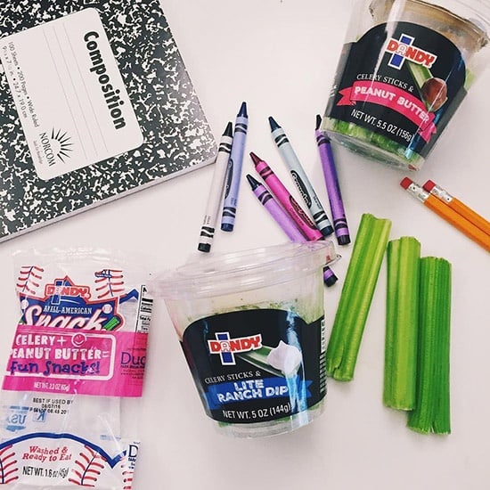 Dandy Celery Sticks and Peanut Butter Snack Cup sitting on a desk with crayons, pencils, and a notebook